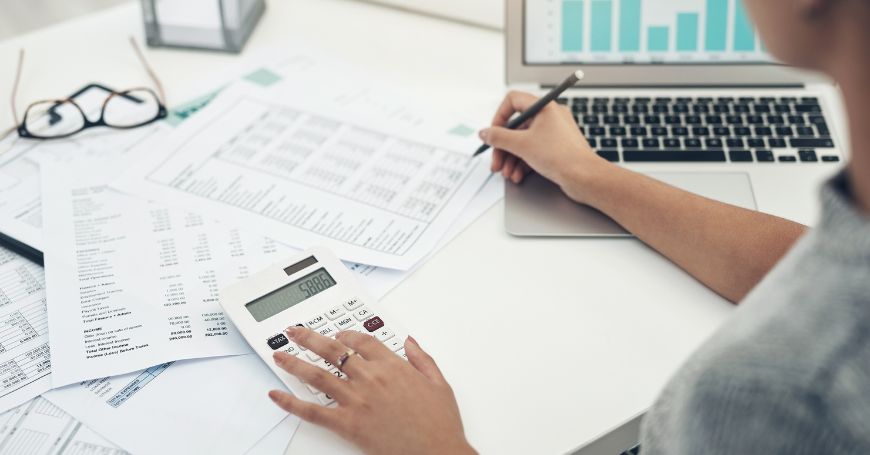 Accountant working on Spain payroll taxes, analyzing financial spreadsheets with a calculator and laptop.