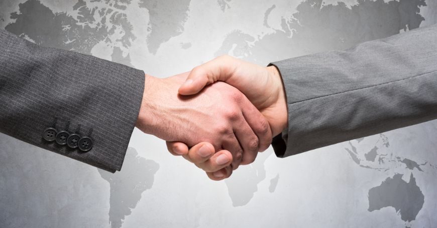 Stretta di mano tra due persone in abiti formali con sfondo di una mappa mondiale, rappresentante l'accordo transfrontaliero nel contesto del regime OSS.