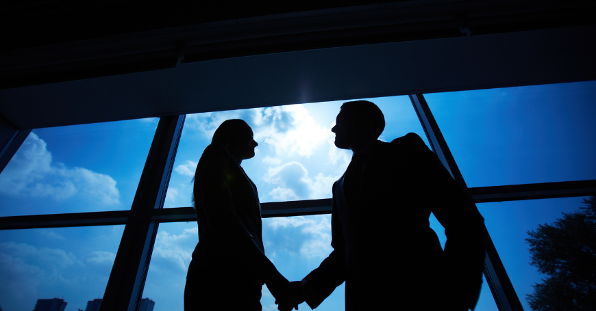 Imprenditori in silhouette si stringono la mano davanti a una vetrata, simbolo di accordo strategico per una società di persone in spagna.